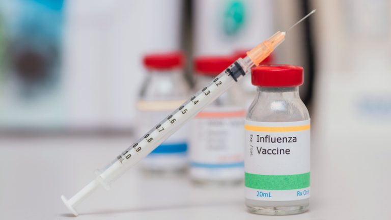 influenza vaccination concept with syringe in vaccine vial and other vials in background